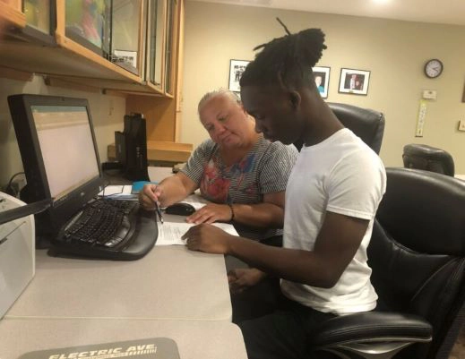 Timothy with Di Tift Di is helping a student sitting at a computer go through a paper in front of him.