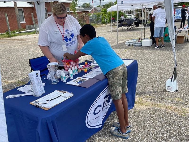 woman at a CILNWF information table at a public awareness event is helping a young man pick swag from a red basket