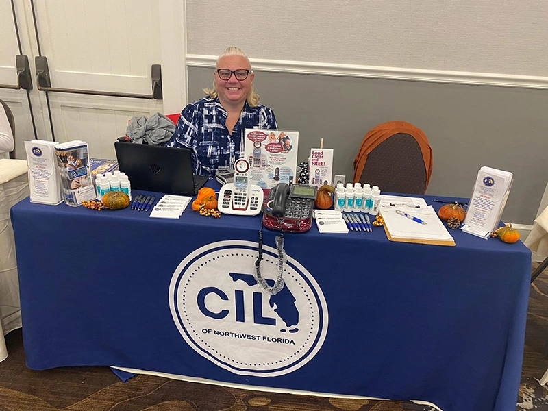 woman smiling behind a table full of CILNWF information, pamphlets, tools, and swag at a public awareness event