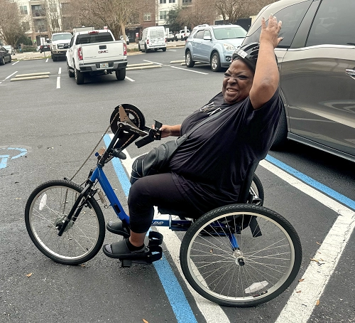 Woman riding a blue handcycle in a parking lot