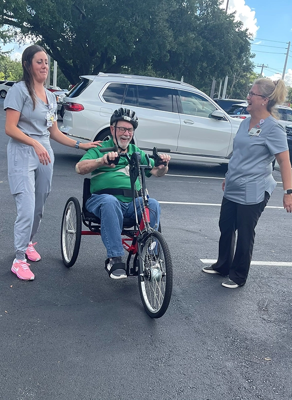 Senior man sitting in a handcycle with two aids in gray uniforms helping him