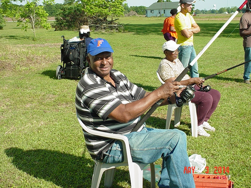 participant sitting in a white plastic lawnchair holding a fishing rod at the Penwheels Fishing Rodeo